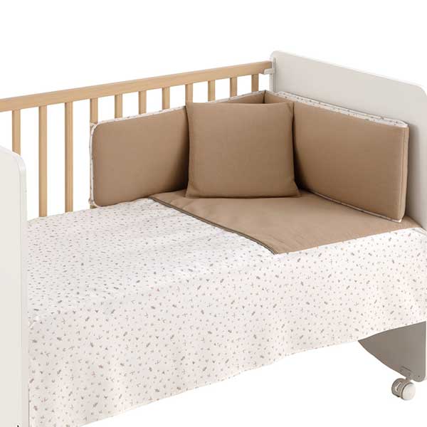 Conjunto textil de cuna de tres piezas de la colección Minimal Beige de Cambrass, que incluye un edredón acolchado de tacto suave, un protector o chichonera a juego para amortiguar los barrotes de la cuna y un cojín decorativo infantil en tonos beige